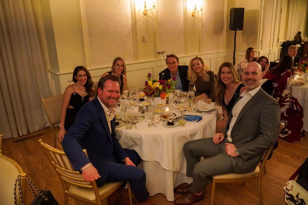 Guests seated around a round banquet table at a formal reception, smiling at the camera.