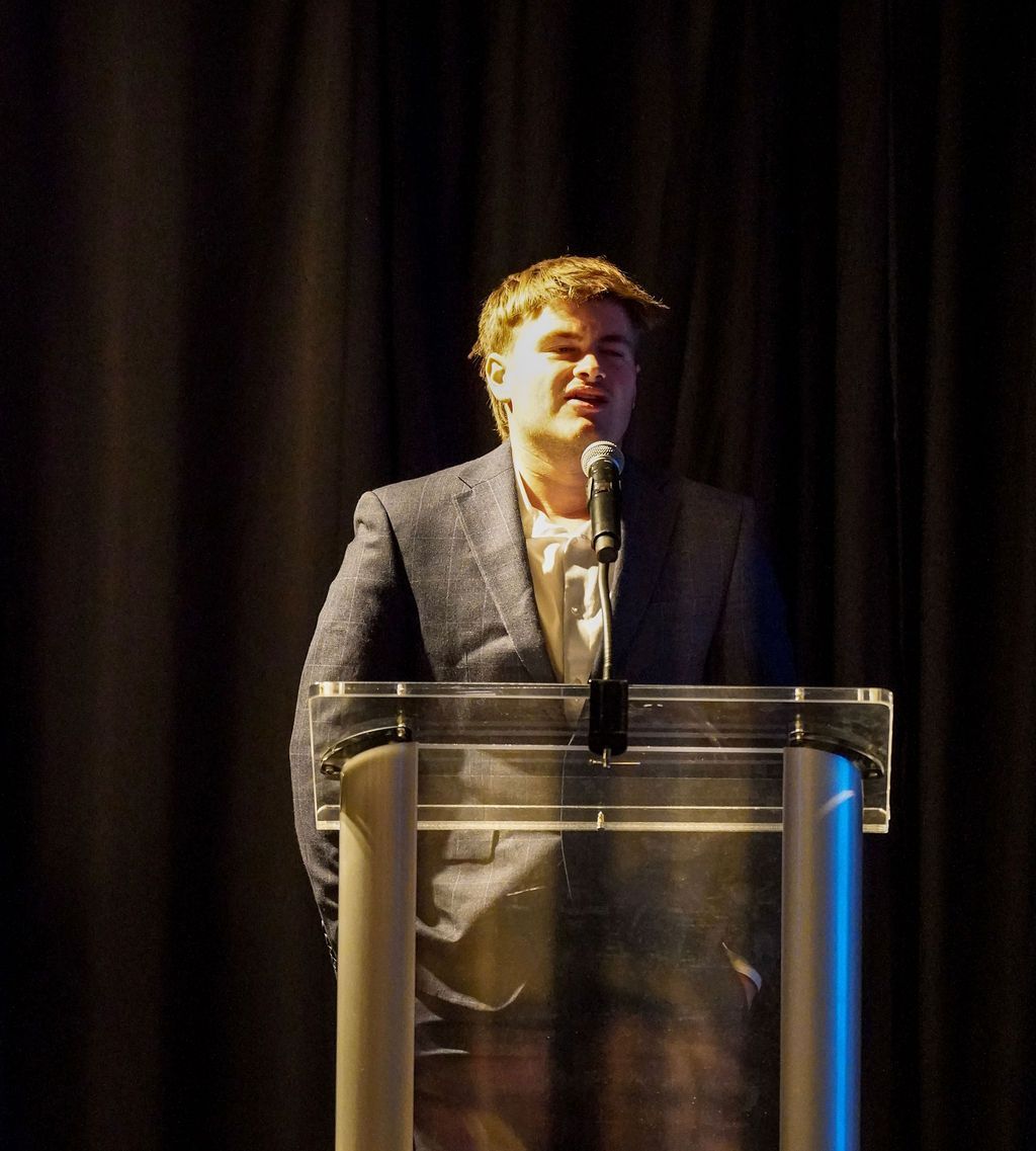 Person speaking at a clear podium on a dimly lit stage