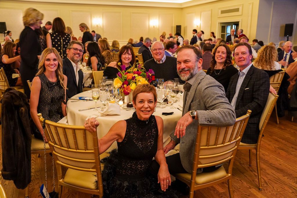 Group of people seated at a banquet table in a warmly lit ballroom, smiling and posing for a photo.