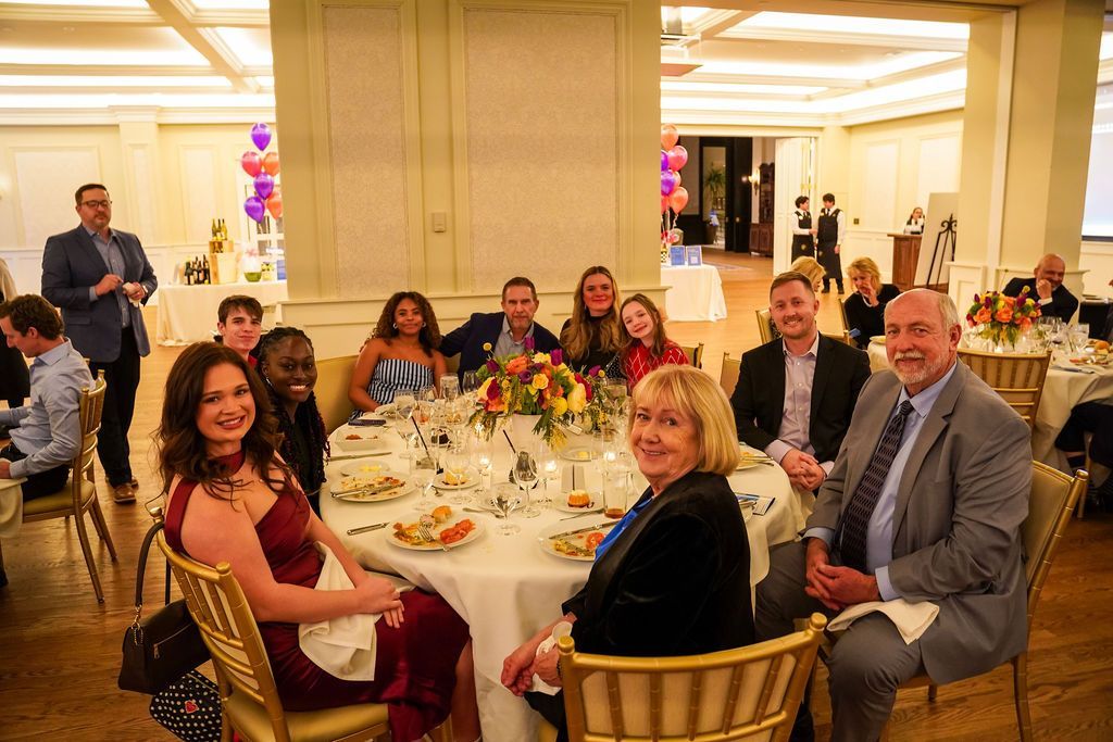 Group seated at a banquet table in a bright ballroom, smiling during a formal event.
