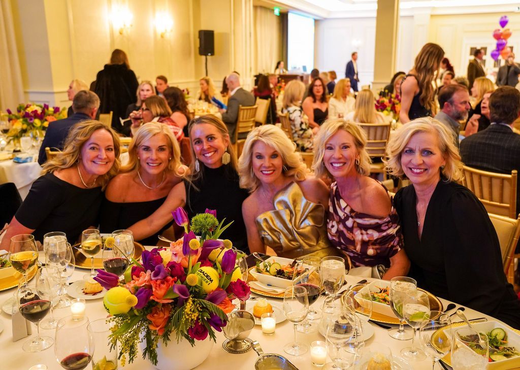 Group of smiling women seated at a decorated banquet table in a warmly lit event hall