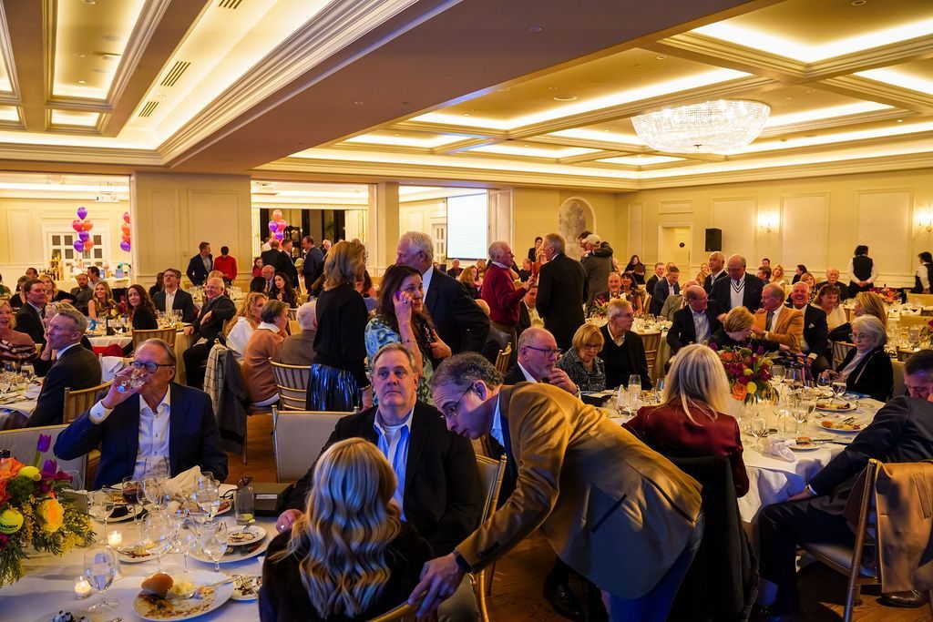 Crowded banquet hall with guests seated at round tables under warm ceiling lights