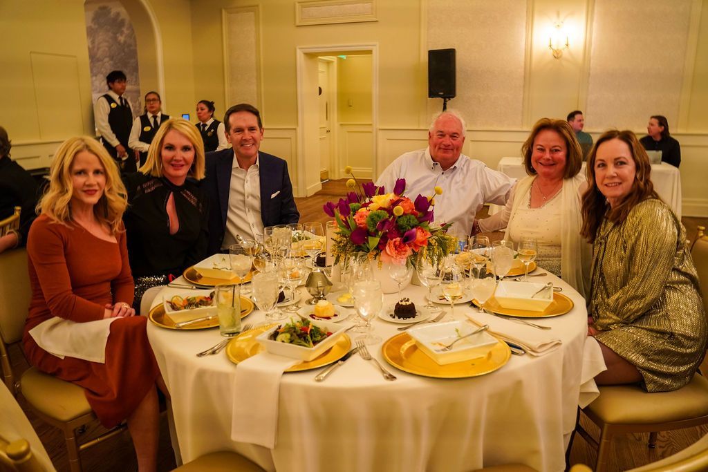 Guests seated around a round banquet table at a formal dinner with flowers and candles
