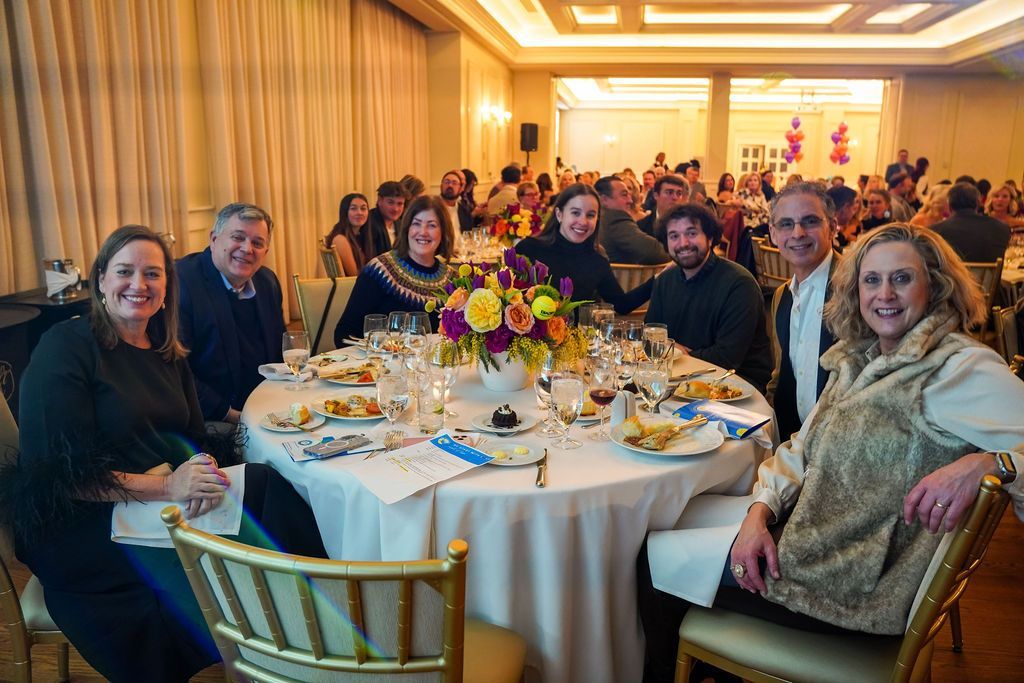 Guests seated around a banquet table in a warmly lit ballroom, smiling for a group photo