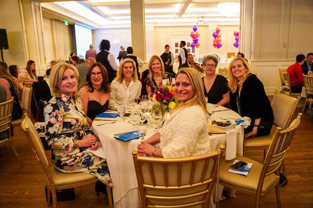 Guests seated at a round table in a bright banquet hall, smiling and chatting at a formal event