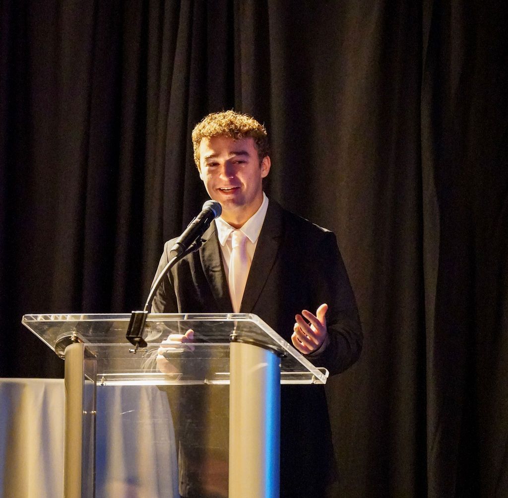 Person speaking at a podium with a microphone on a dimly lit stage