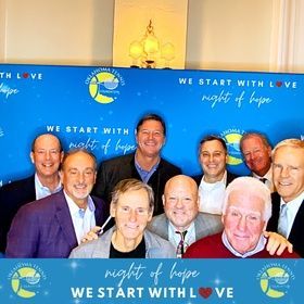 Group of smiling people posing before a blue “We Start With Love” and “night of hope” event backdrop