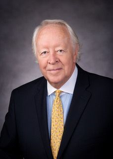 Studio portrait of Judge Mike McSpadden in a dark suit, blue shirt, and gold tie against a gray backdrop