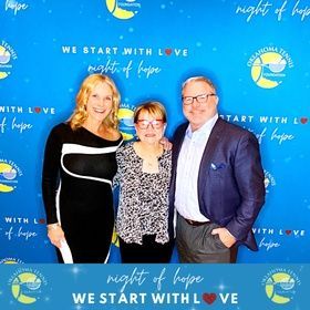 Three people posing at a blue “Night of Hope” event backdrop with “We start with love” text