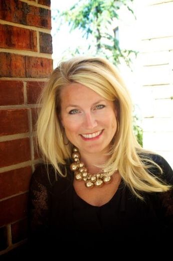 Executive Director Carmen Bond in a black top and gold necklace, standing beside a brick wall outdoors.