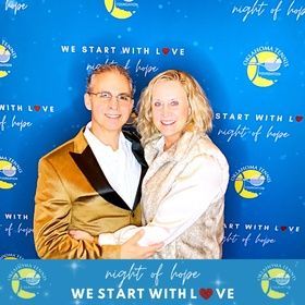 Two people posing together at a “Night of Hope” event backdrop in blue and gold.