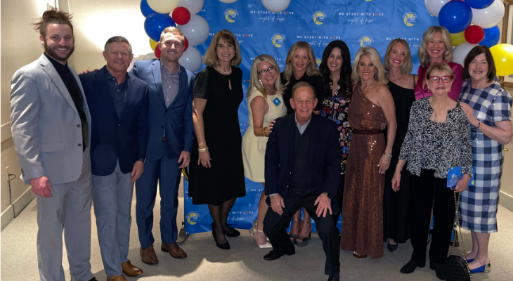 Group of people posing at a formal event with blue, red, and white balloon decorations.