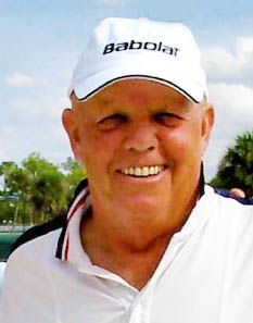 Smiling person in a white Babolat cap and polo shirt outdoors under a blue sky