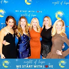 Five women posing at a “Night of Hope” event backdrop with blue and yellow logos.