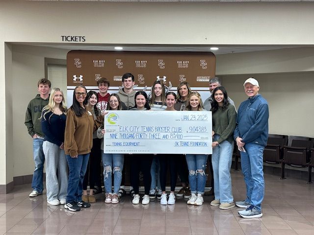 Group holding a large check at a school ticket office counter, posing for a photo.