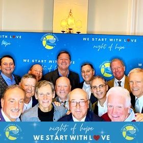 Group of smiling men posing before a blue “We Start with Love / night of hope” event backdrop