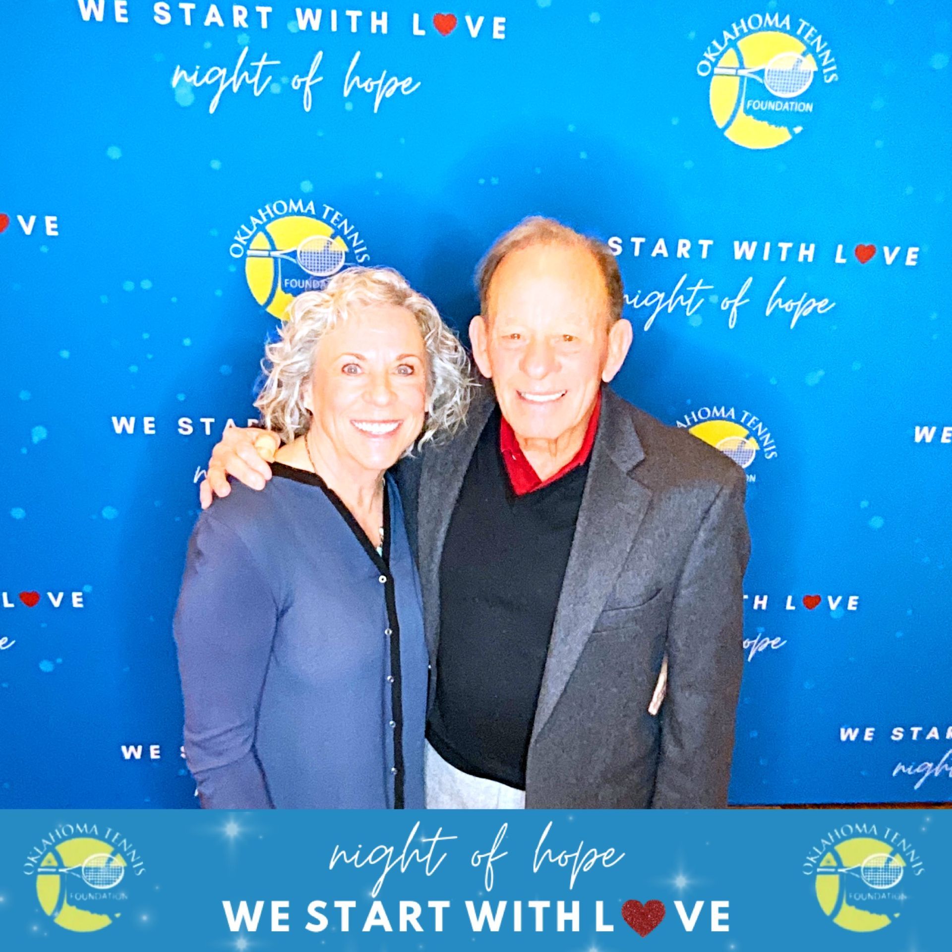 Two smiling people posing before a blue “We Start With Love” Night of Hope backdrop