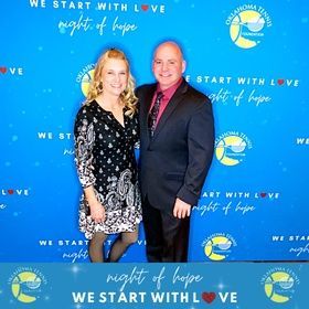 Two people posing on a blue “We Start with Love” event backdrop, with a “Night of Hope” logo.
