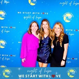 Three women posing at a blue “Night of Hope” event backdrop, smiling in colorful dresses.