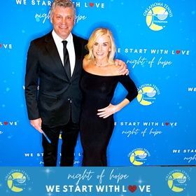 Two people posing on a blue “Night of Hope” step-and-repeat backdrop, dressed in black formal wear.