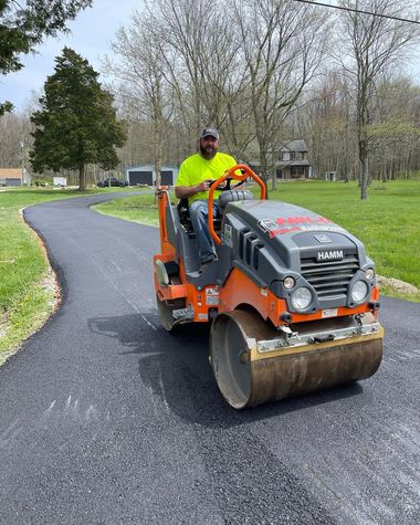 Worker operating a road roller on a curving paved path in a park
