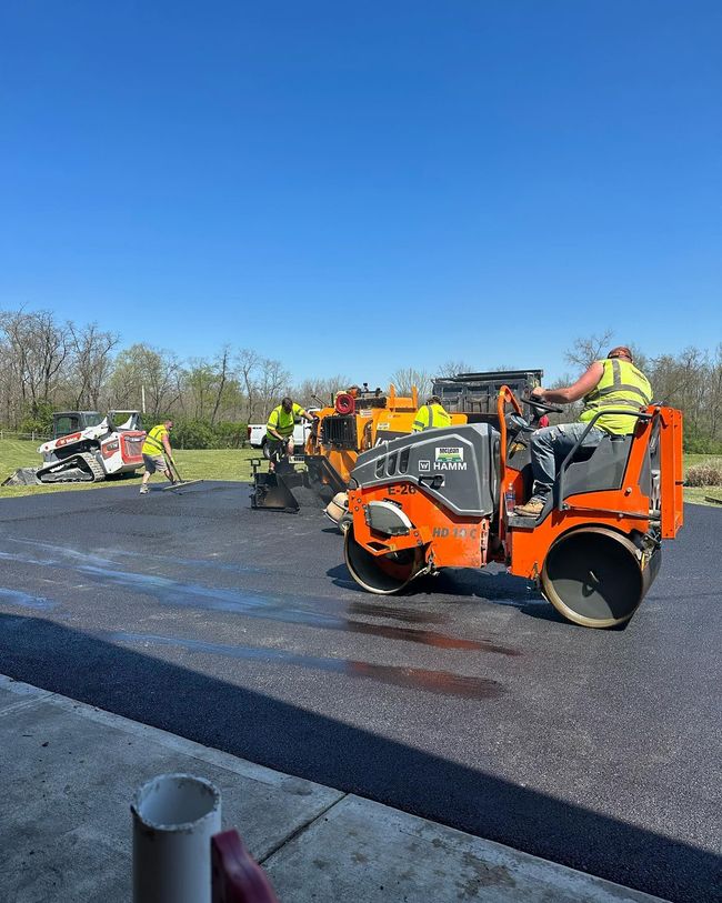 Orange construction equipment and workers on a gravel road under a clear blue sky