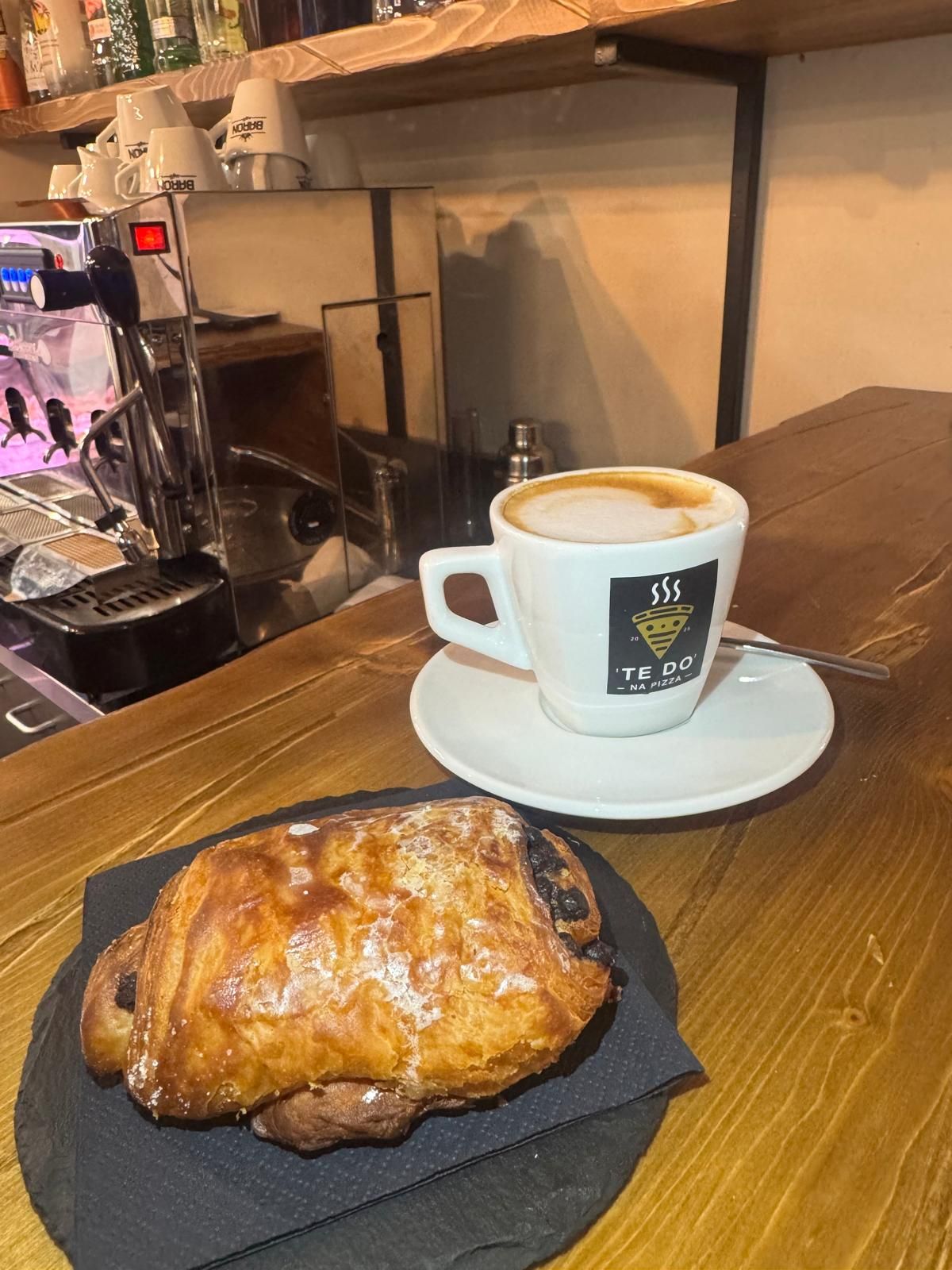 Cappuccino in una tazza bianca con un pasticcino sul bancone di un bar.