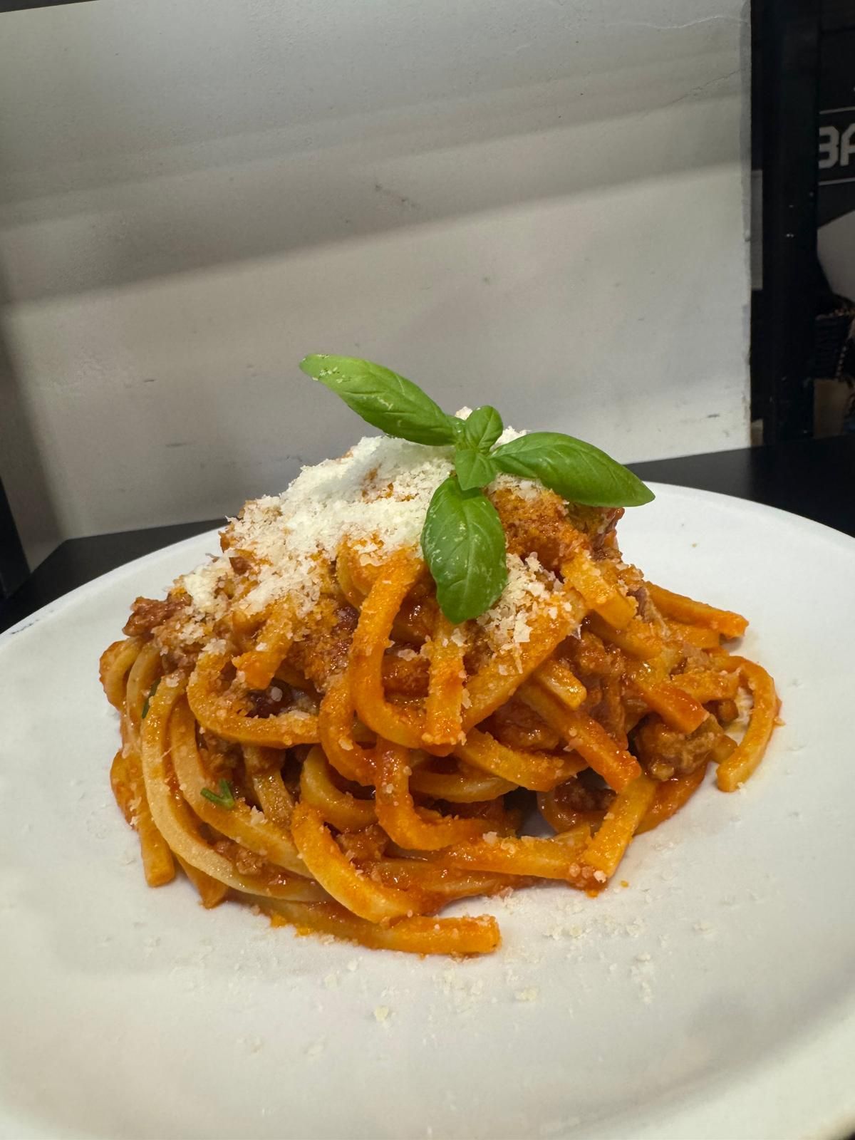 Piatto di spaghetti con salsa di pomodoro, formaggio grattugiato e guarnizione di basilico.