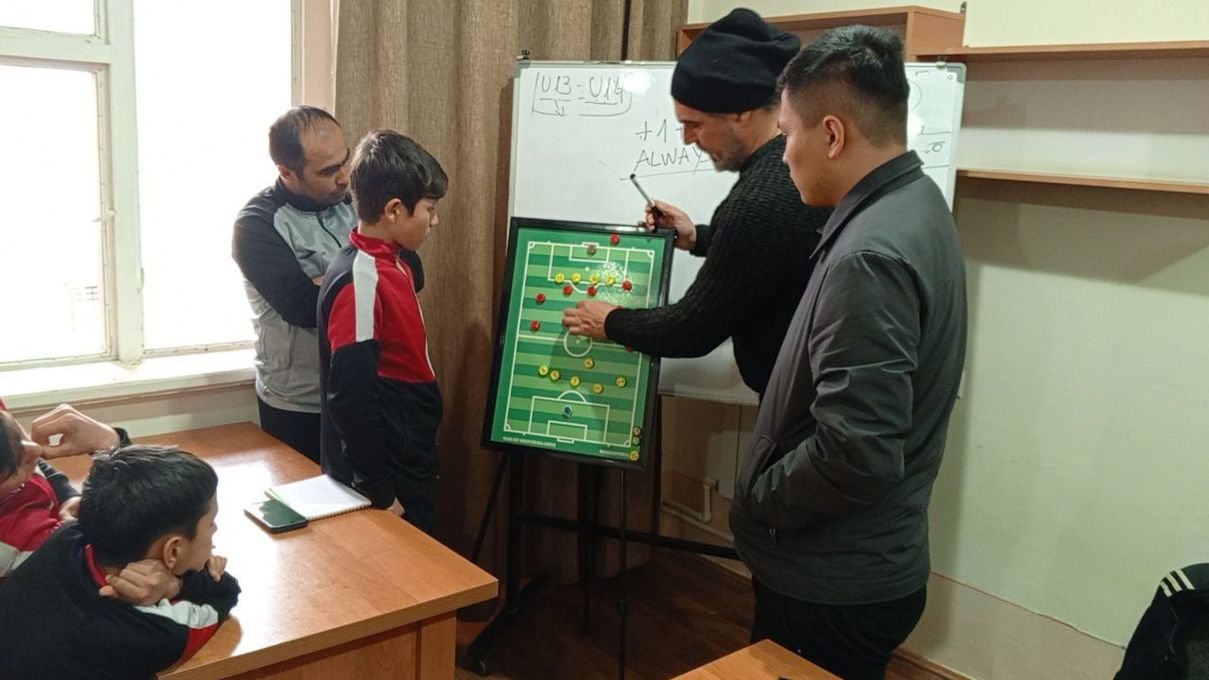 Un'insegnante indica una lavagna verde mentre gli studenti la osservano in classe.