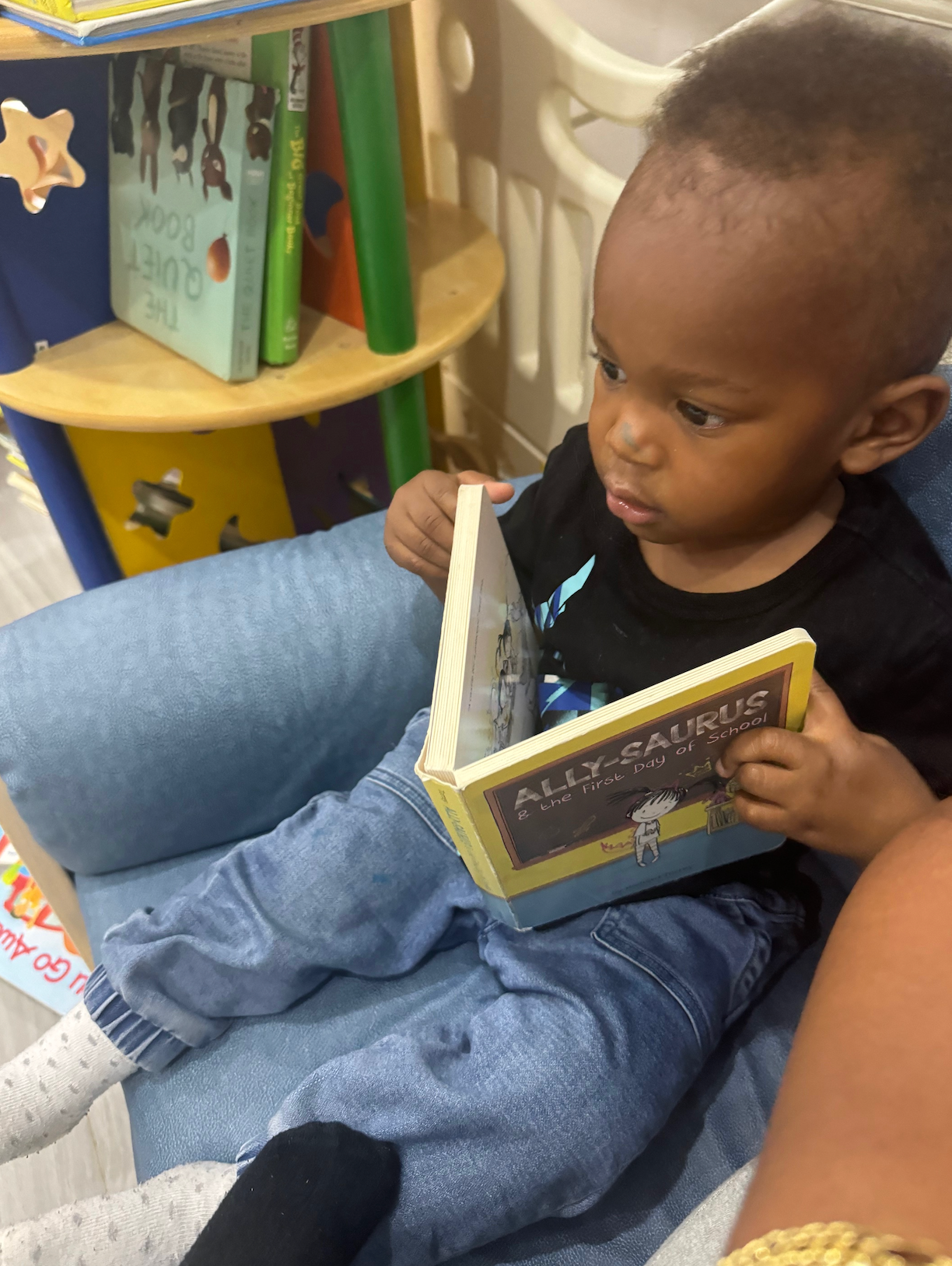 A baby is sitting in a chair reading a book called ally calmus