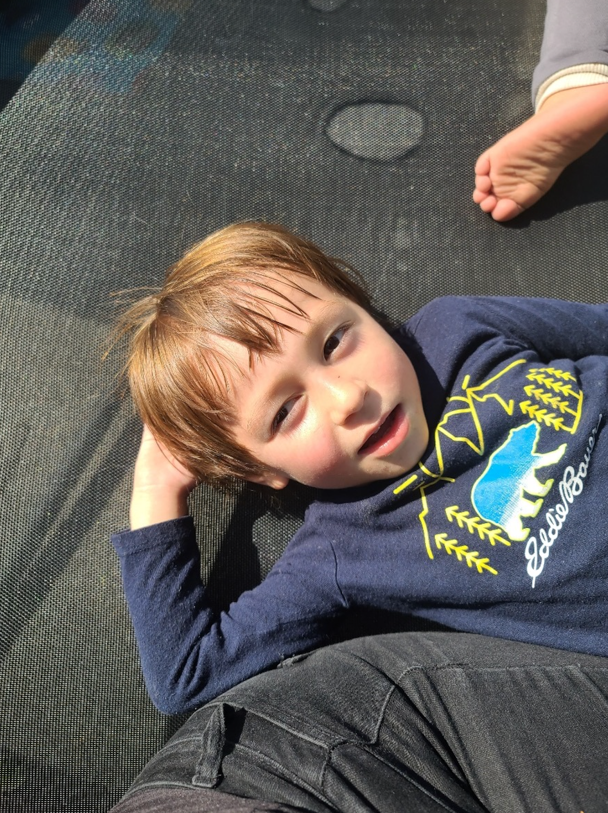 A young boy in a blue shirt is laying on a trampoline.