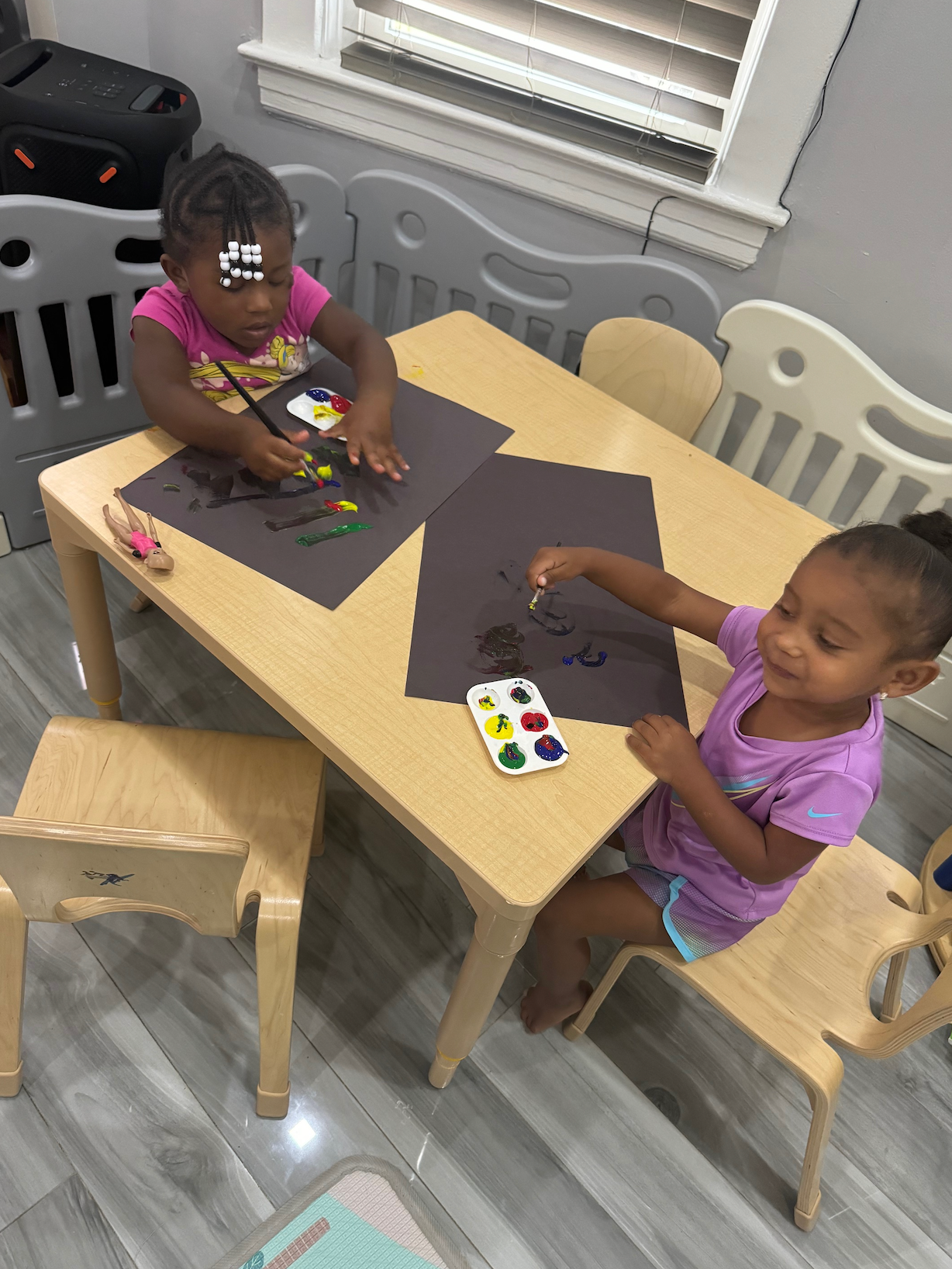 Two little girls are sitting at a table painting with watercolors.