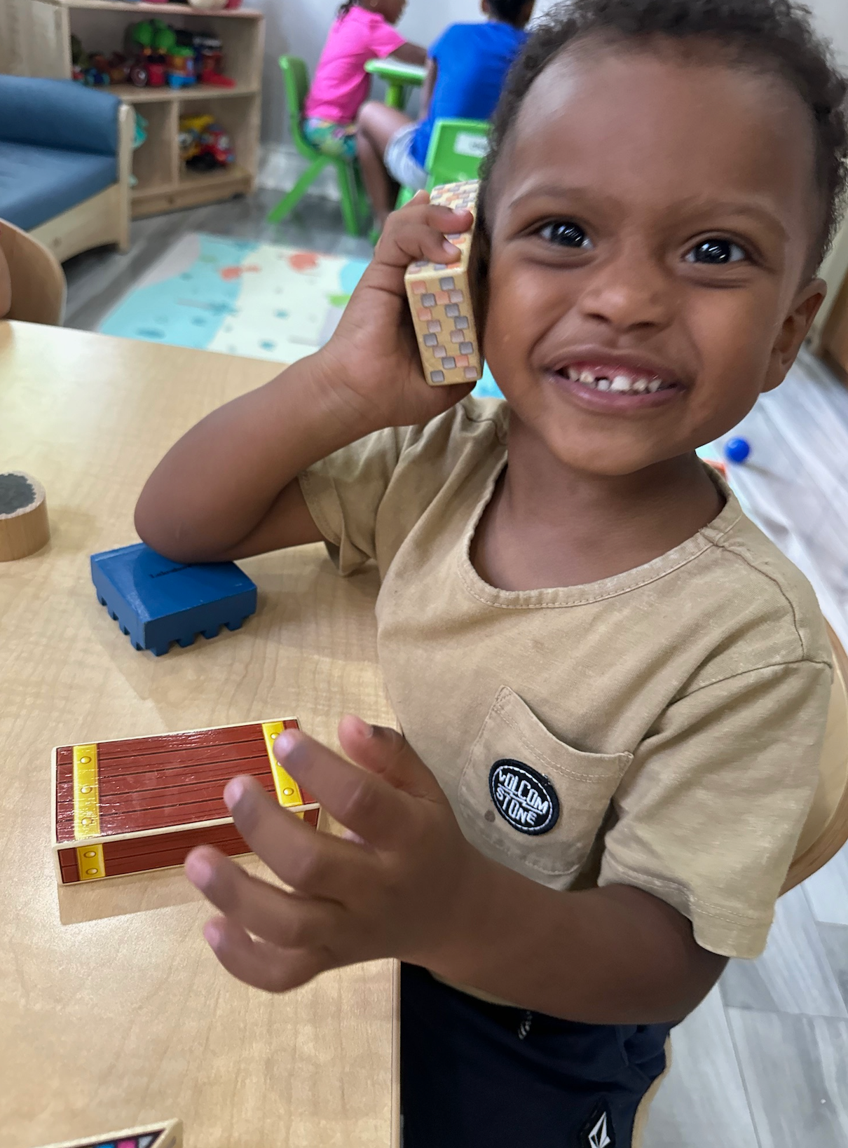 A young boy is sitting at a table holding a wooden block.