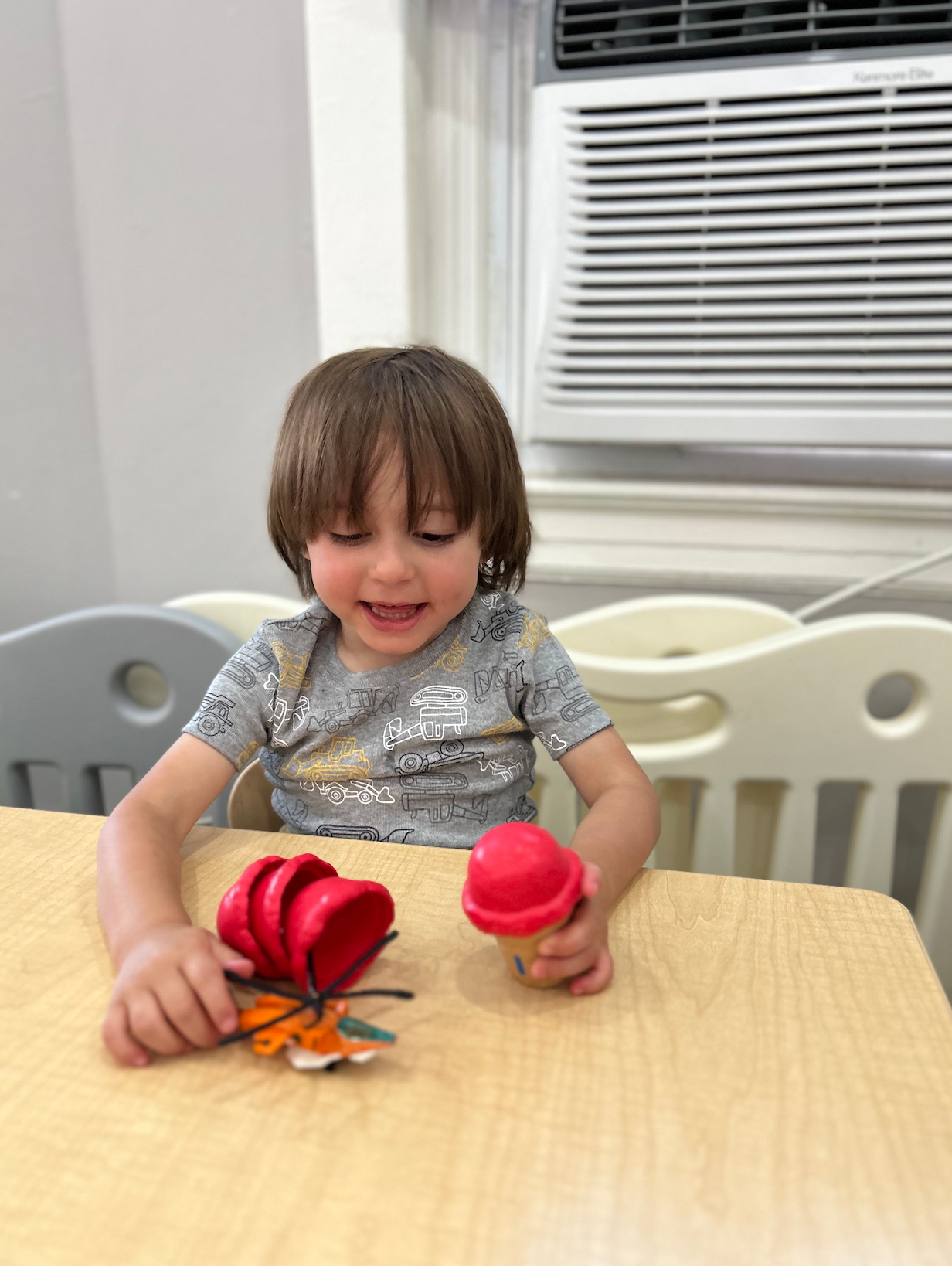 A little girl is sitting at a table playing with a red toy.