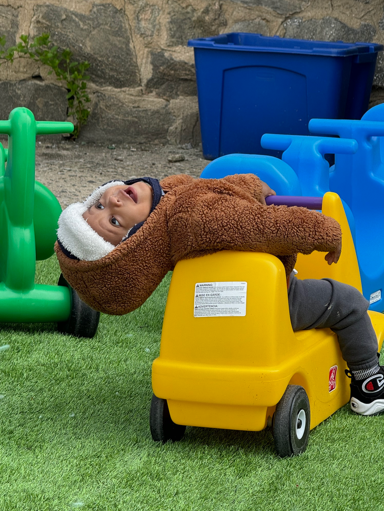 A little boy is laying on top of a yellow toy truck.