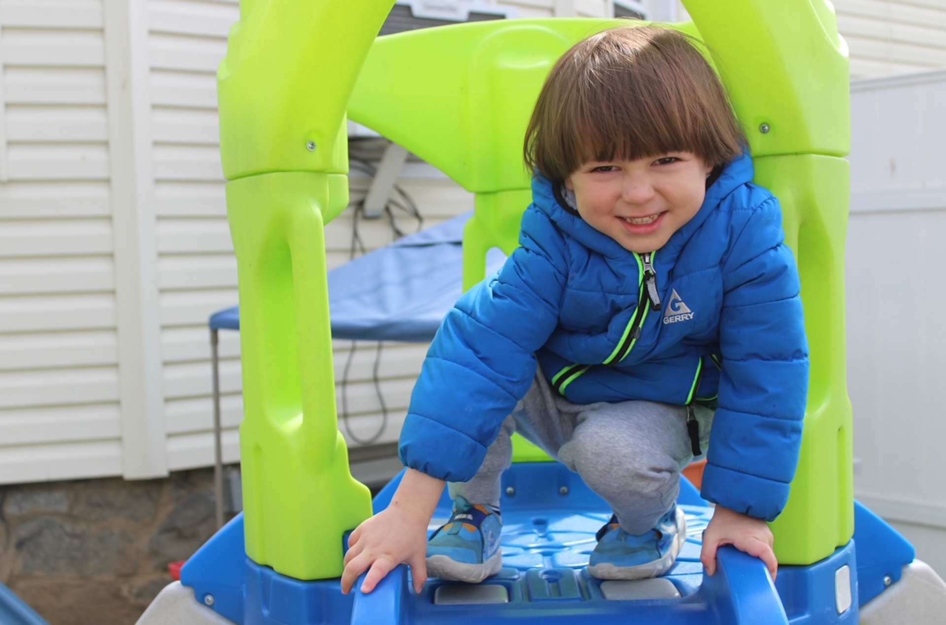 A young boy in a blue jacket is playing on a slide.