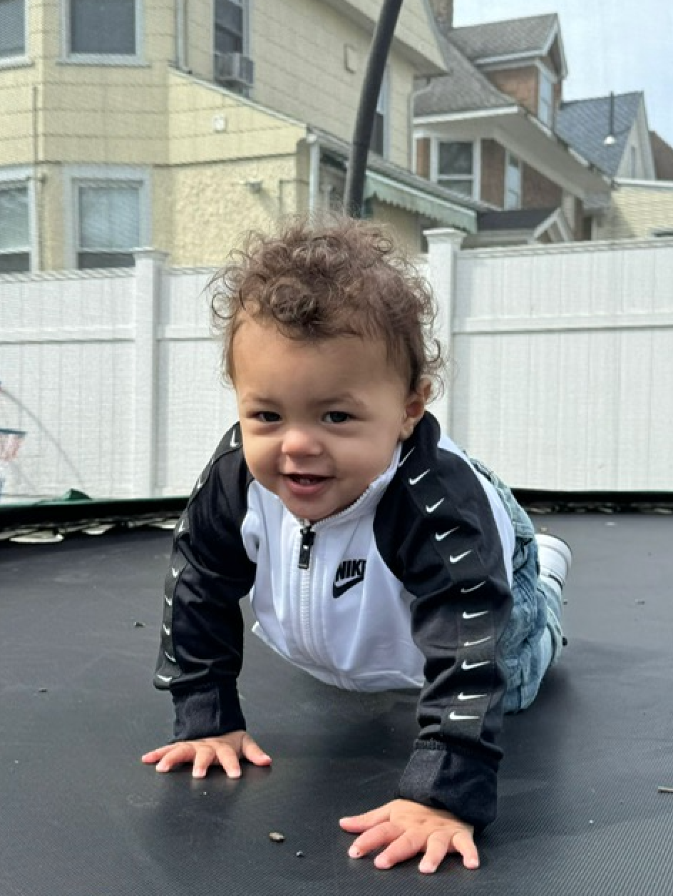 A baby wearing a nike jacket is crawling on a trampoline