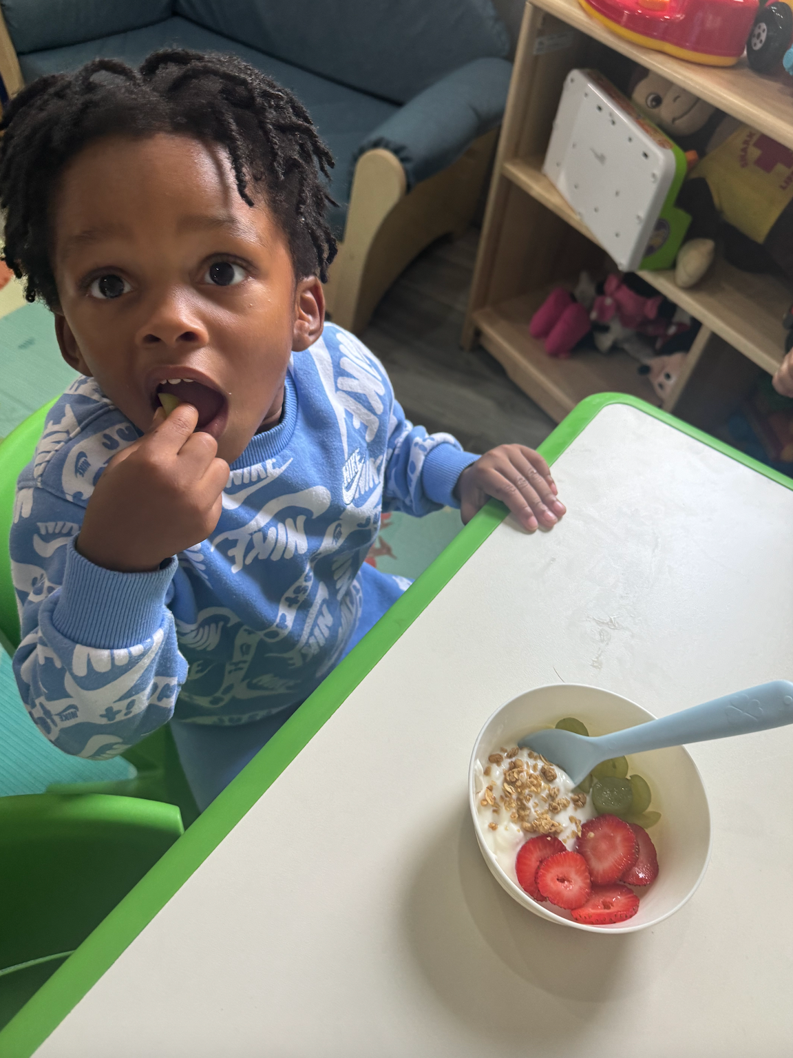 A young boy is sitting at a table with a bowl of strawberries and yogurt