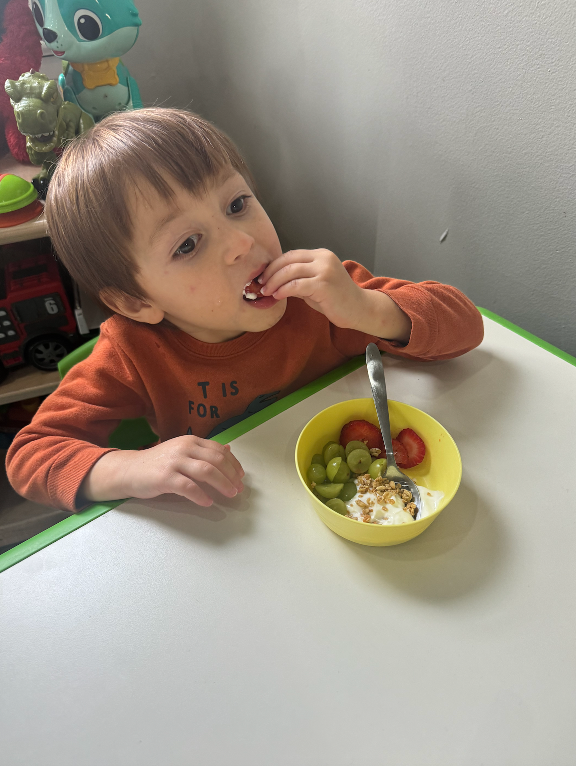 A young boy is sitting at a table eating a bowl of fruit.