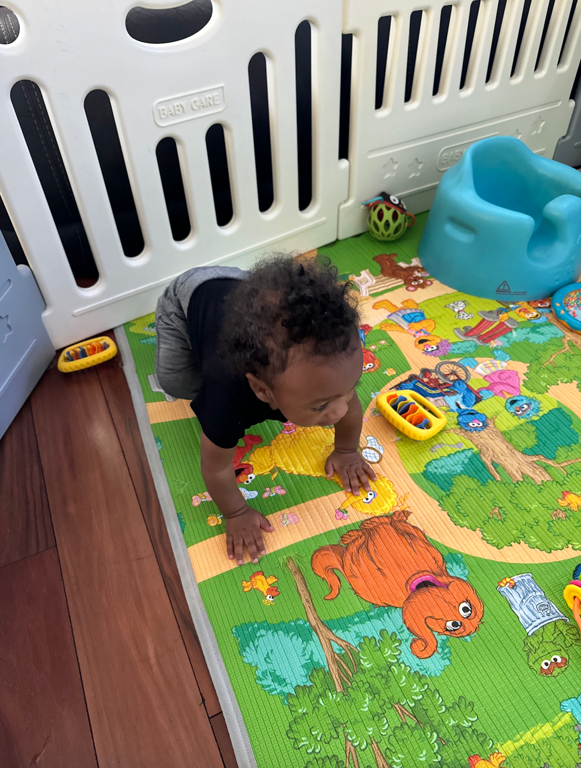 A baby is crawling on a play mat next to a fence.