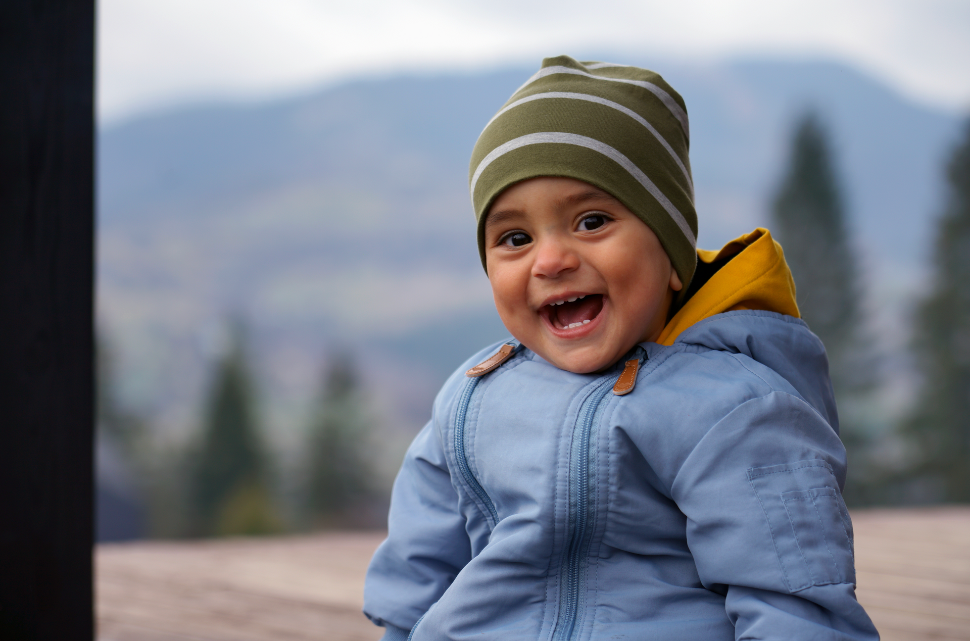 A little boy wearing a blue jacket and a green hat is smiling.
