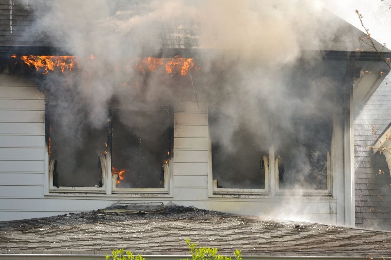 House engulfed in flames, billowing smoke from windows and roof.