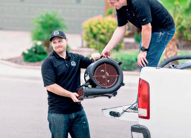Two men are loading a blower into the back of a truck.