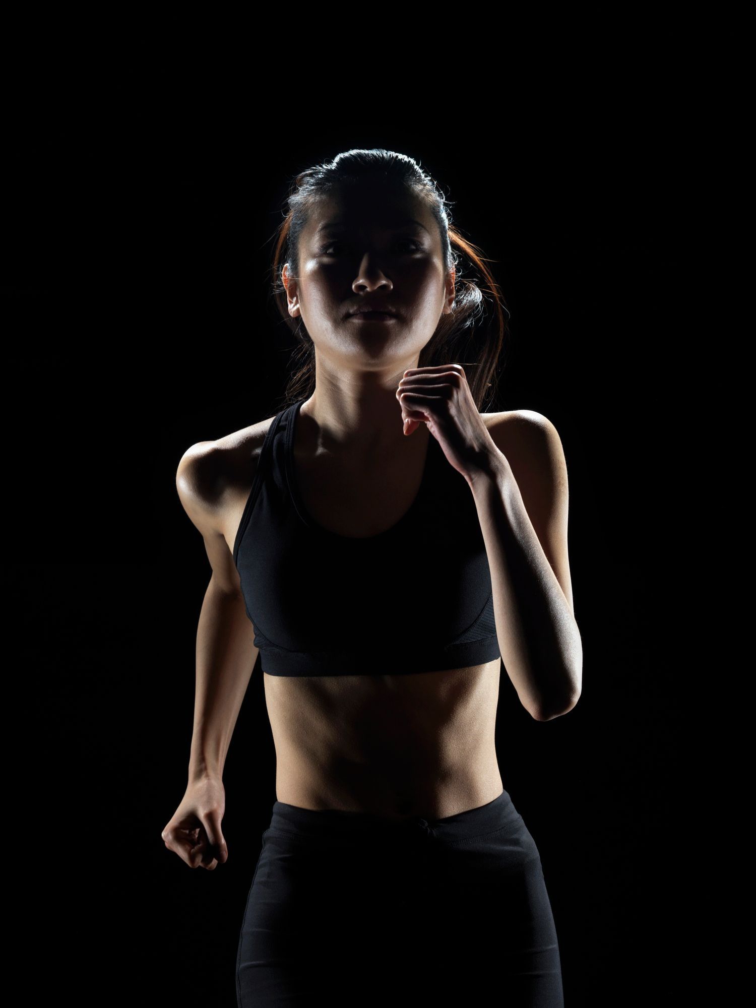 Backlit athlete in black sportswear jogging against a dark background