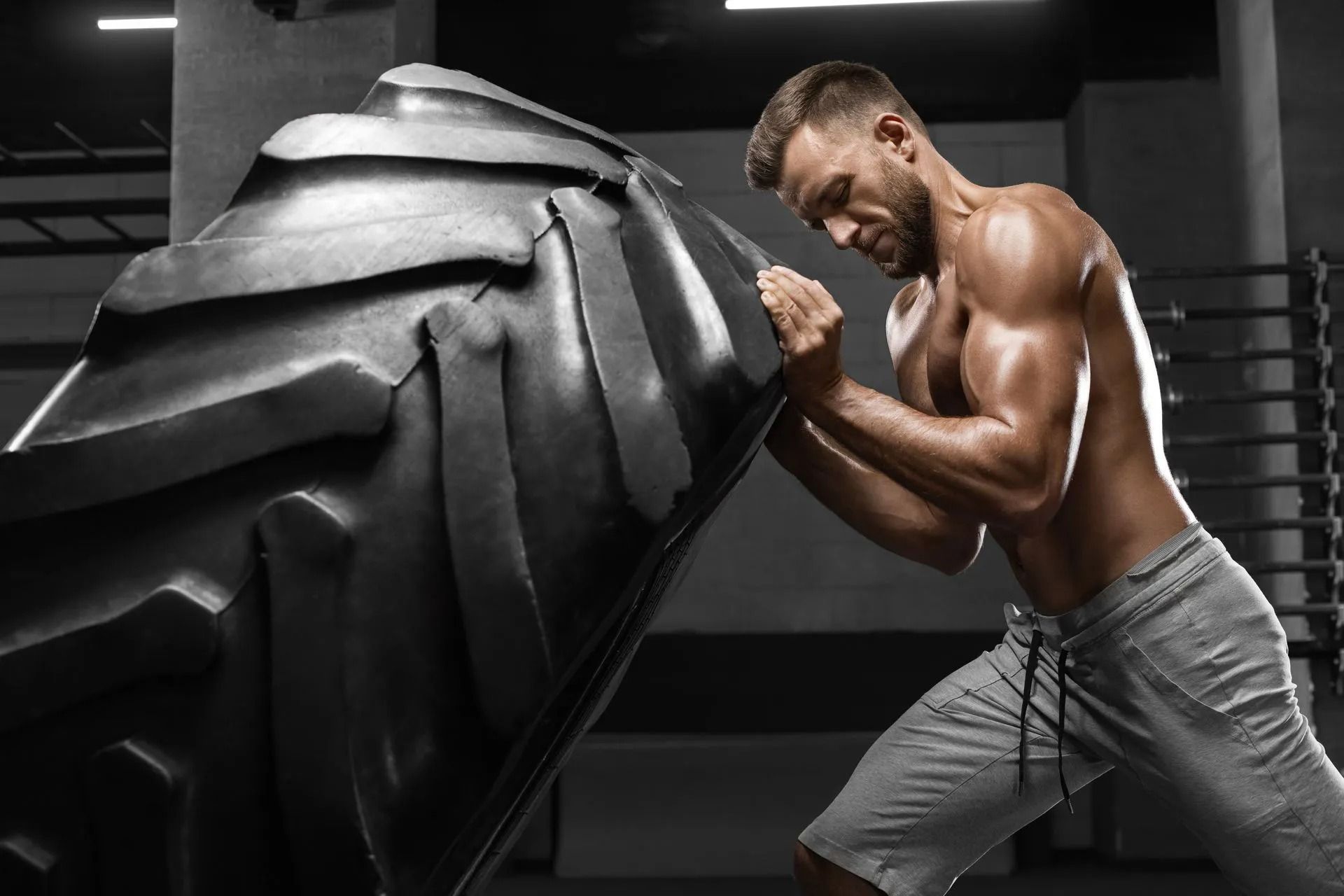 Man pushing a large tire in a gym, straining with effort.