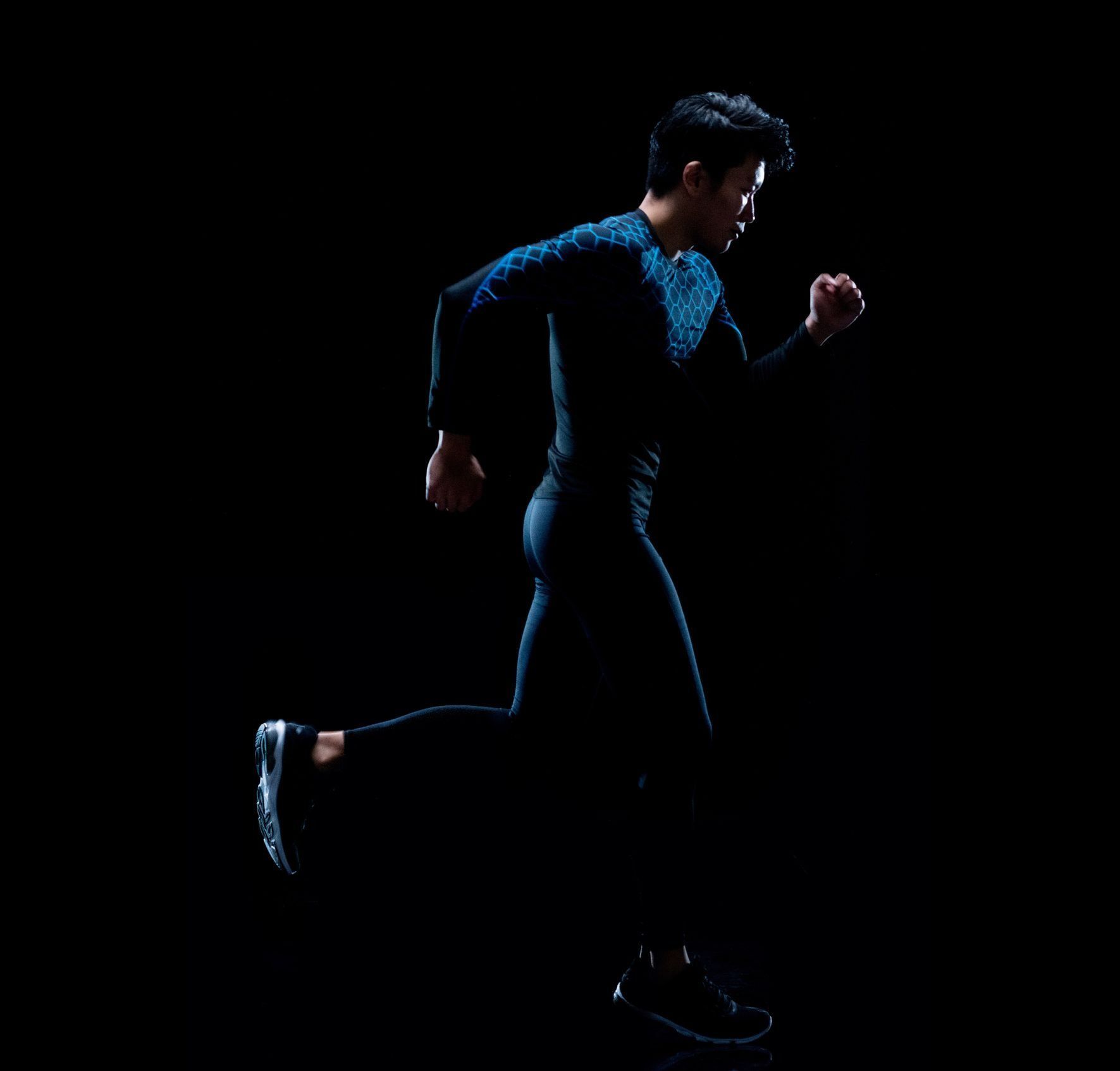 A runner in dark blue athletic gear sprinting against a black background