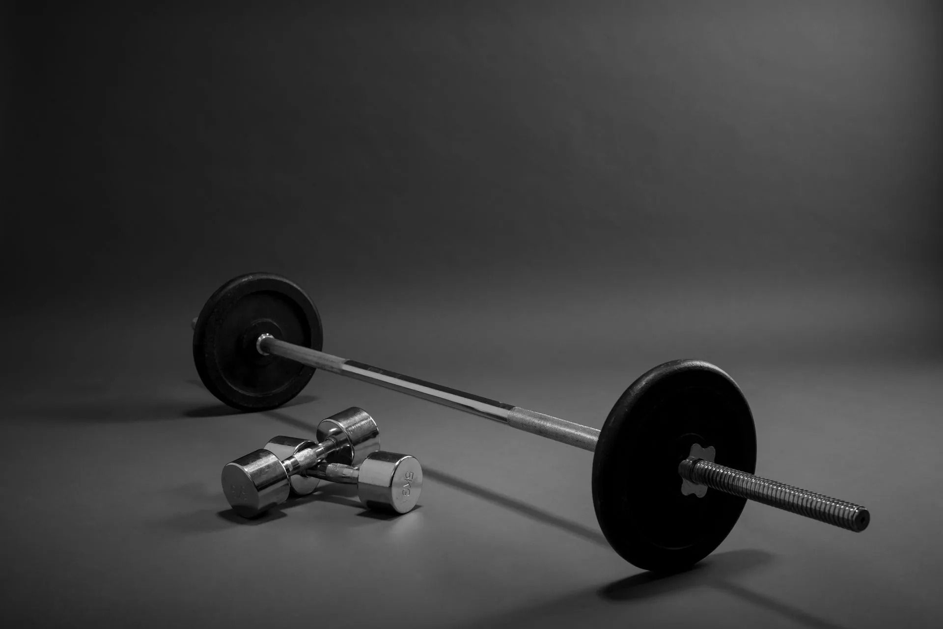 Barbell with black weight plates and dumbbells on a gray studio floor