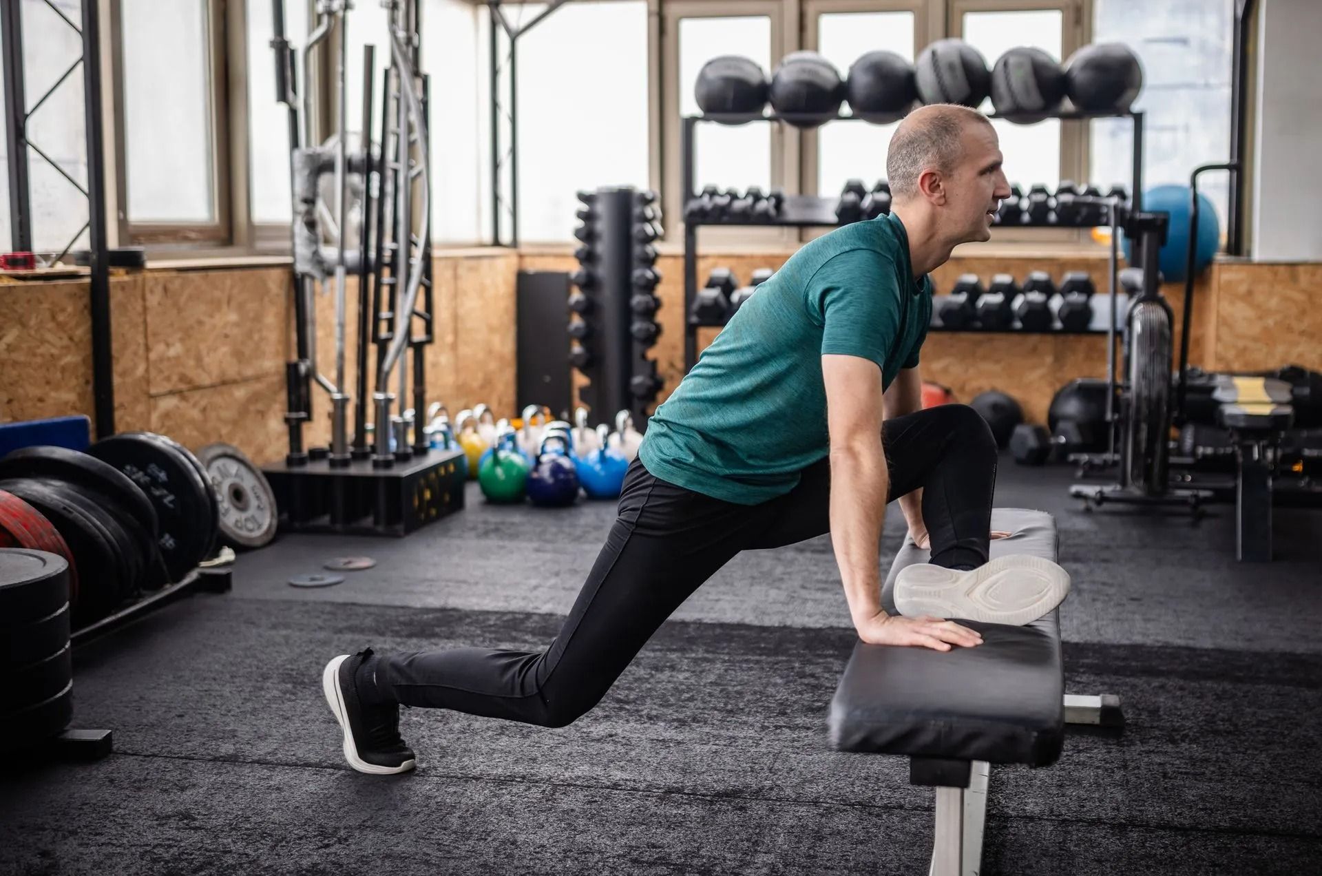 Person stretching on a bench in a gym, with kettlebells and dumbbells in the background