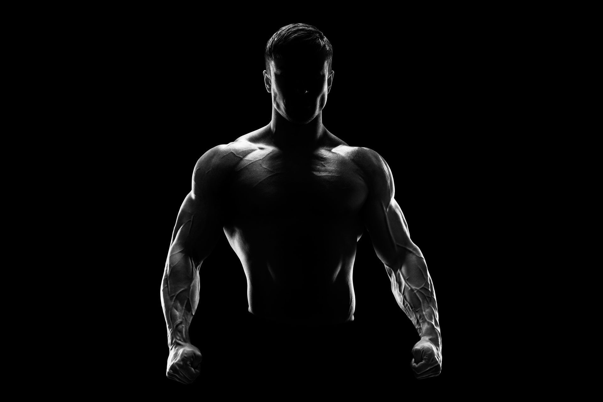 Silhouetted muscular man against a black background, lit from behind, fists clenched.