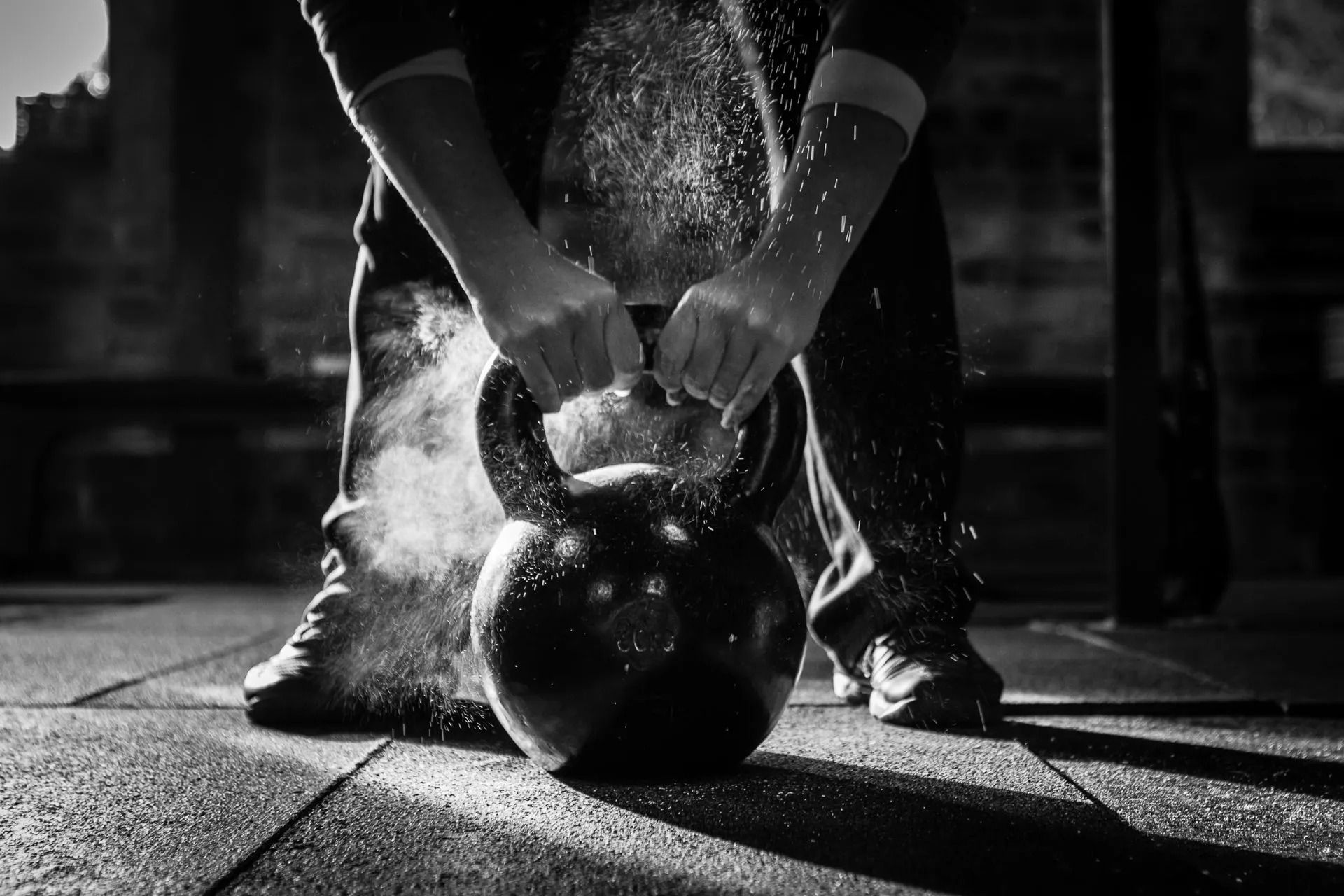Person gripping a kettlebell on a gym floor, with chalk dust in black and white.